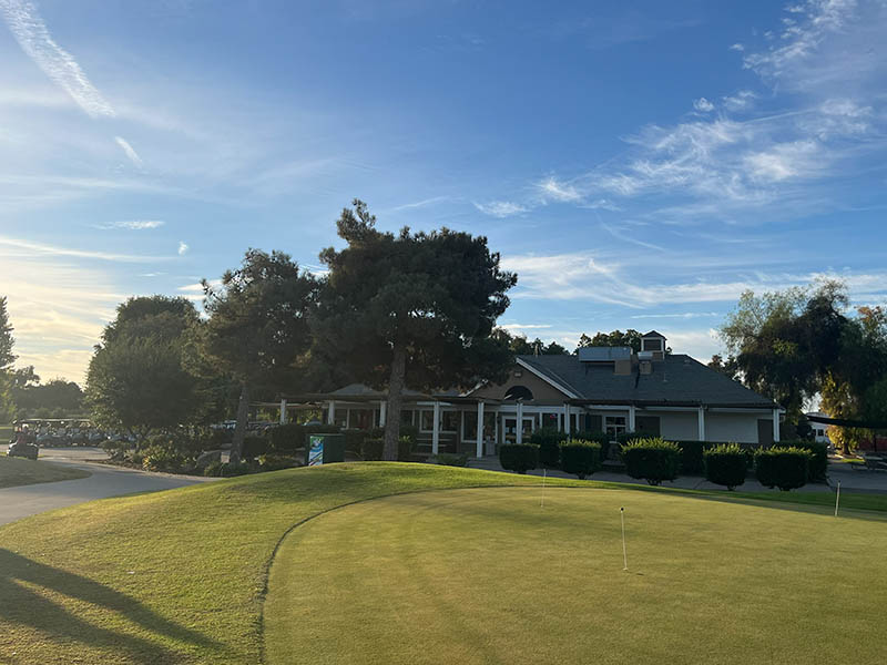 Lemoore Golf Course clubhouse and practice green with golf carts, trees, and sunny course views.