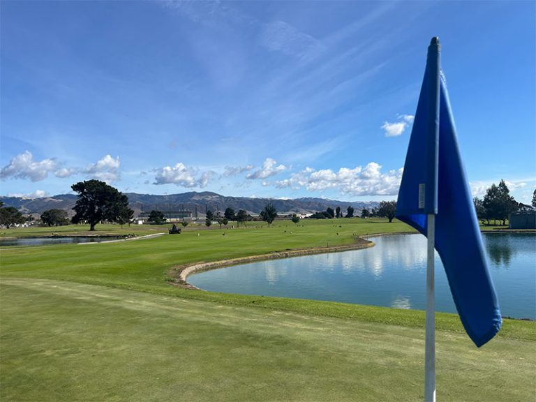 Golf green with a blue flag beside a pond and mountain views at Salinas Fairways Golf Course.
