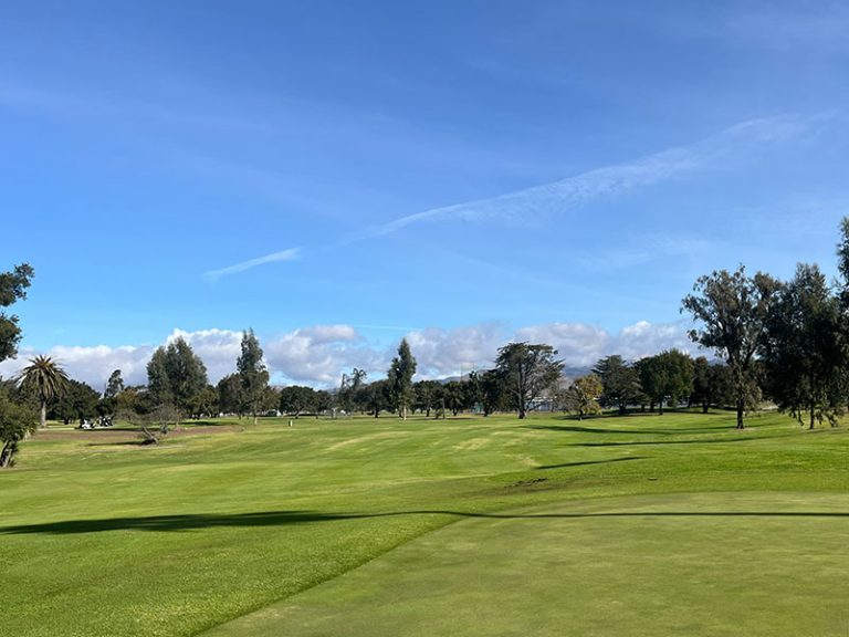 Expansive green fairway surrounded by mature trees beneath a bright blue California sky.